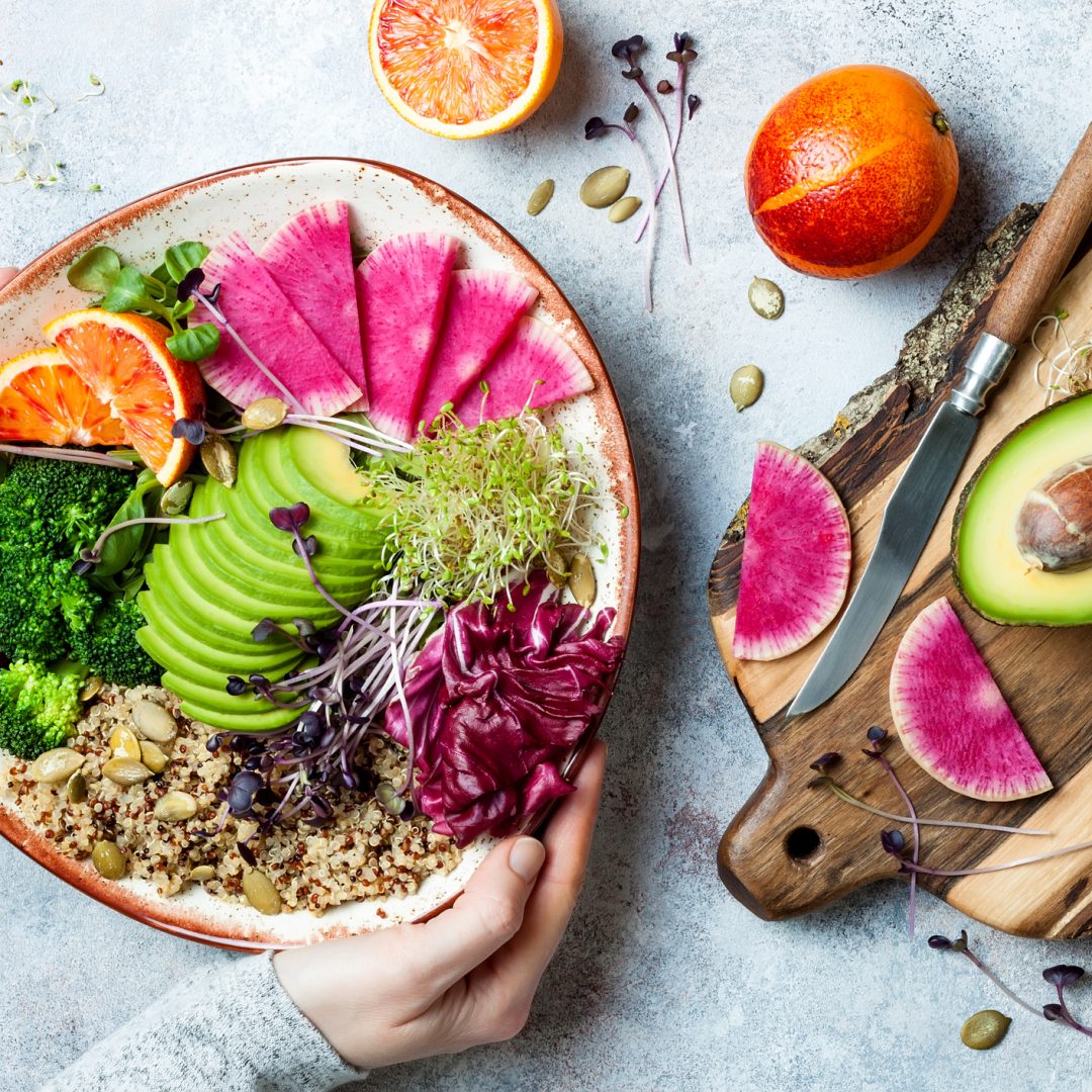 Girl holding vegan, detox Buddha bowl with quinoa, micro greens, avocado, blood orange, broccoli, watermelon radish, alfalfa seed sprouts.